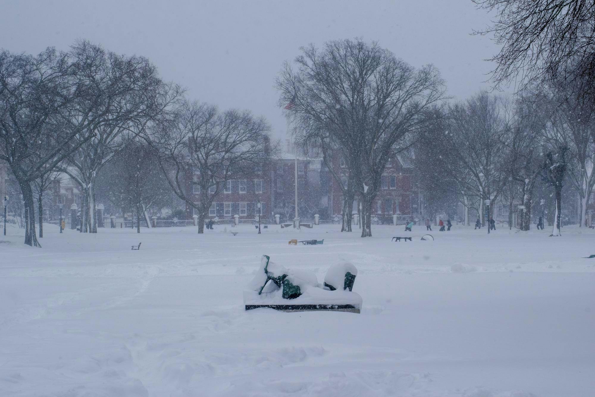 A photo of the Main Green covered in snow during a blizzard with scattered chairs and people in the background.
