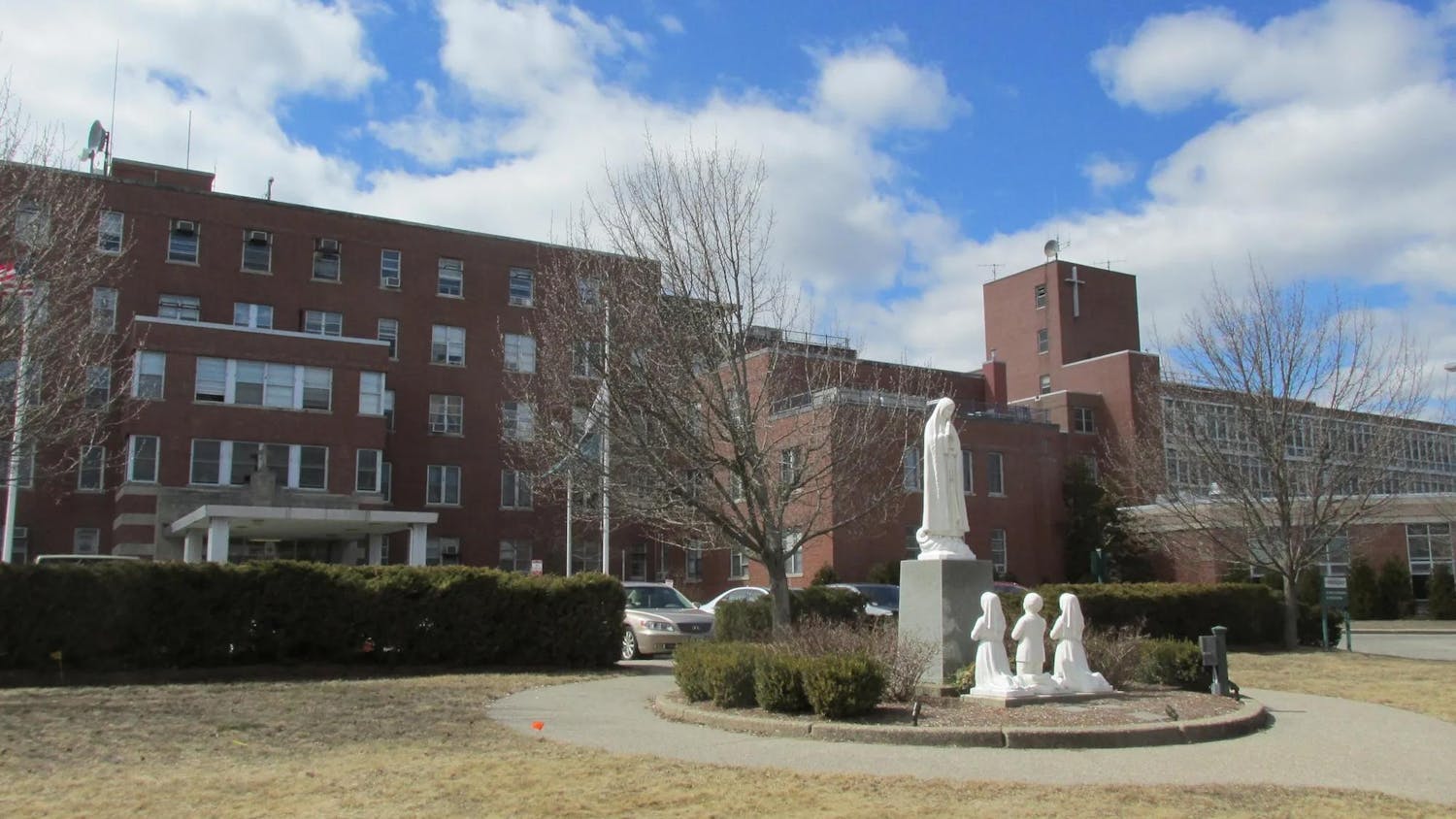 Photo of large brick building with a dry grass field and statue in front.