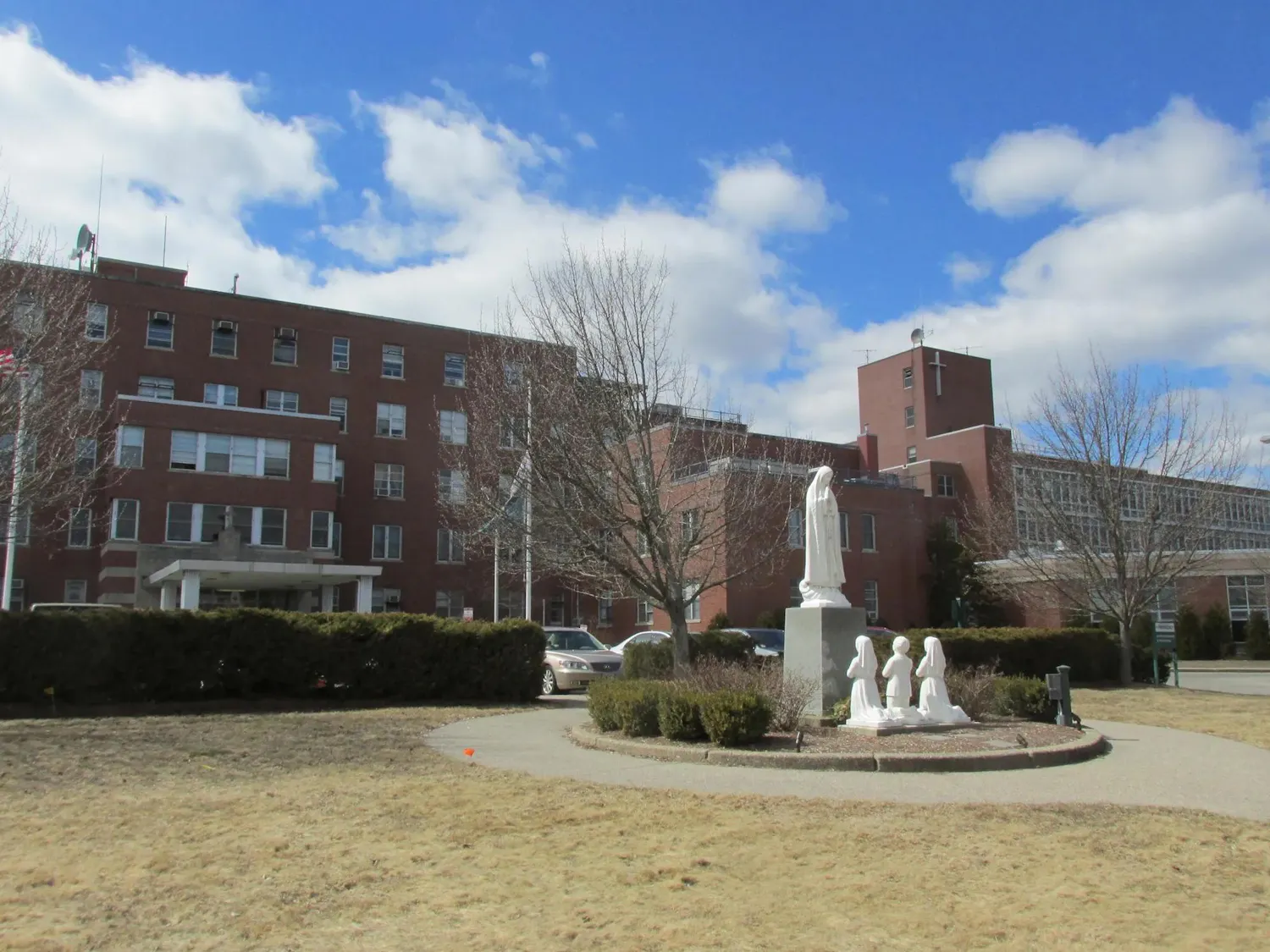 Photo of large brick building with a dry grass field and statue in front.