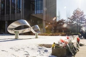 Photo of the silver infinity statue outside Barus and Holley, aglow with sunlight, with bouquets of flowers on a ledge in front of it.