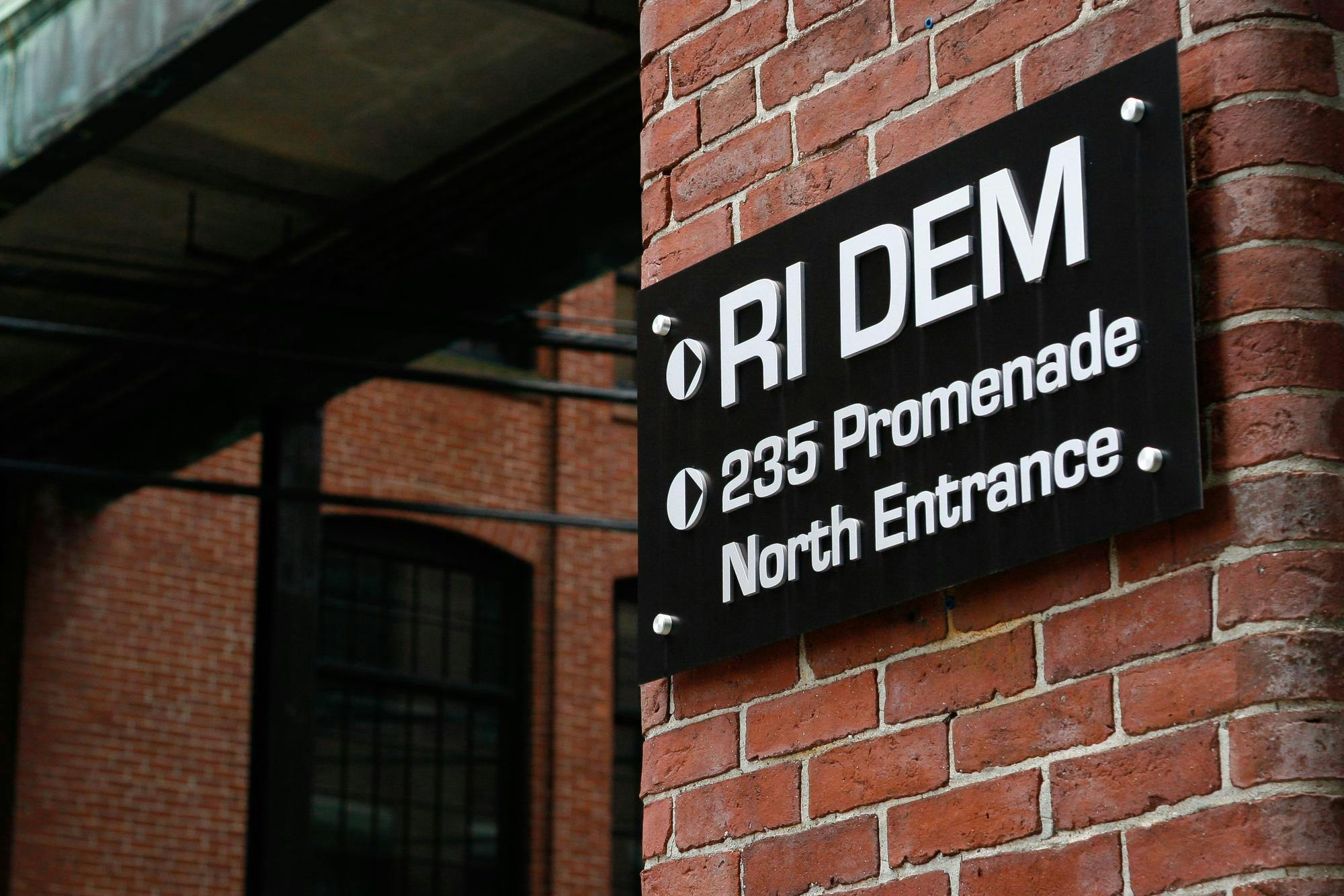 Photograph of a sign on a brick wall reading "RI DEM 235 Promenade North Entrance"