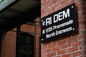 Photograph of a sign on a brick wall reading "RI DEM 235 Promenade North Entrance"