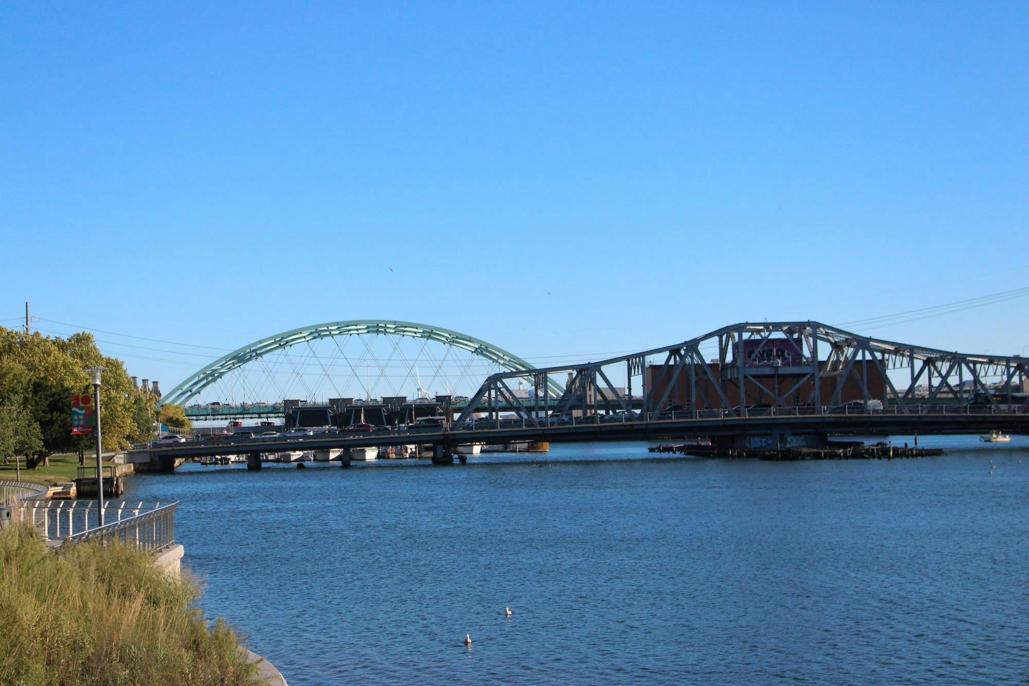 Photo of two bridges over the Providence River. The one in the back is shaped like a green semicircle and the one in the front is a grey trapezoid.