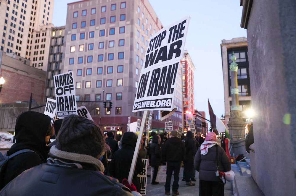 A protestor holds up a sign and walks through a street alongside many other protestors holding similar signs.