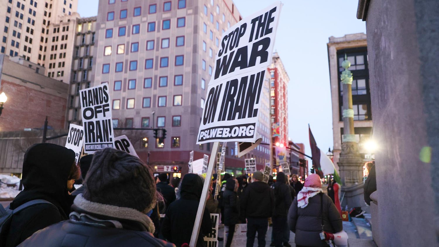 A protestor holds up a sign and walks through a street alongside many other protestors holding similar signs.