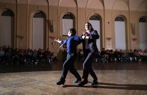A student and a professor dancing together in a large ballroom.