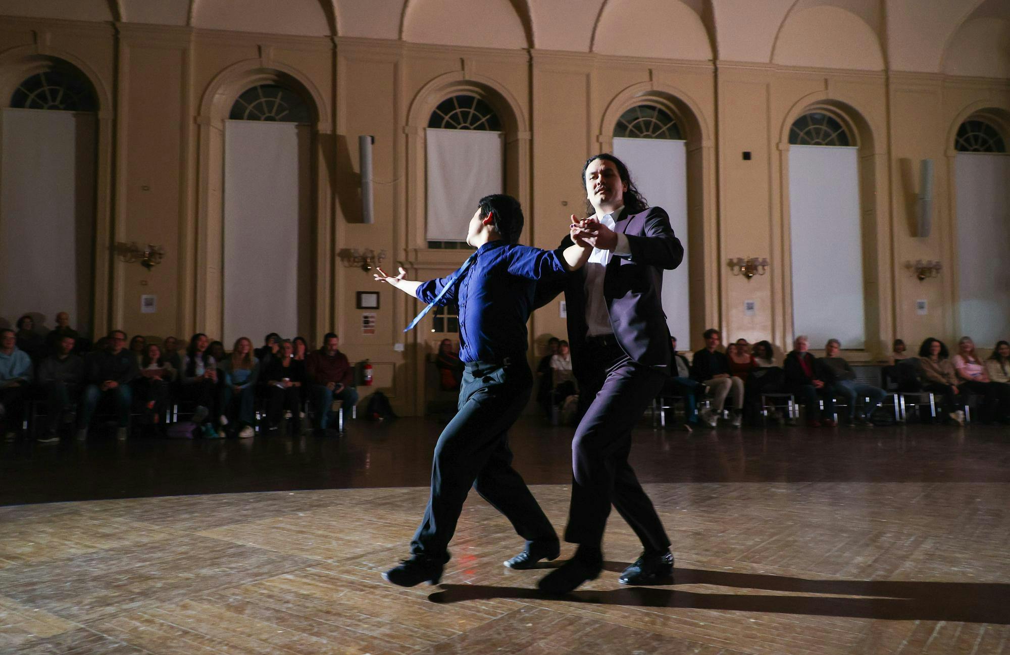 A student and a professor dancing together in a large ballroom.
