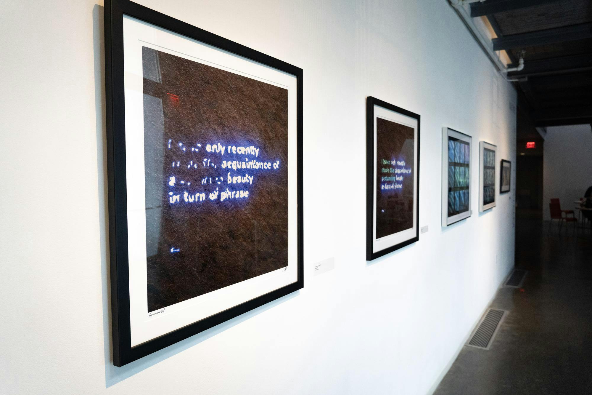 A photo of framed images showing neon word signs hung on a white wall.
