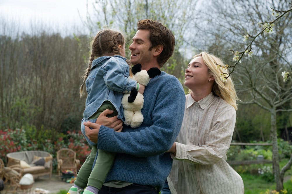 A photo of a man (Andrew Garfield) holding a child followed by a woman (Florence Pugh).