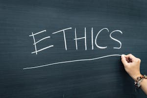 Photo of a person writing "ETHICS" on a chalkboard.