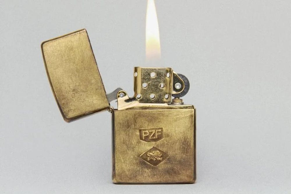 A close-up photo of a lit gold Zippo lighter, with the letters PZF engraved on it.

