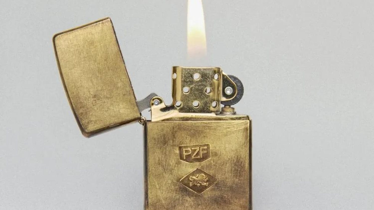 A close-up photo of a lit gold Zippo lighter, with the letters PZF engraved on it.