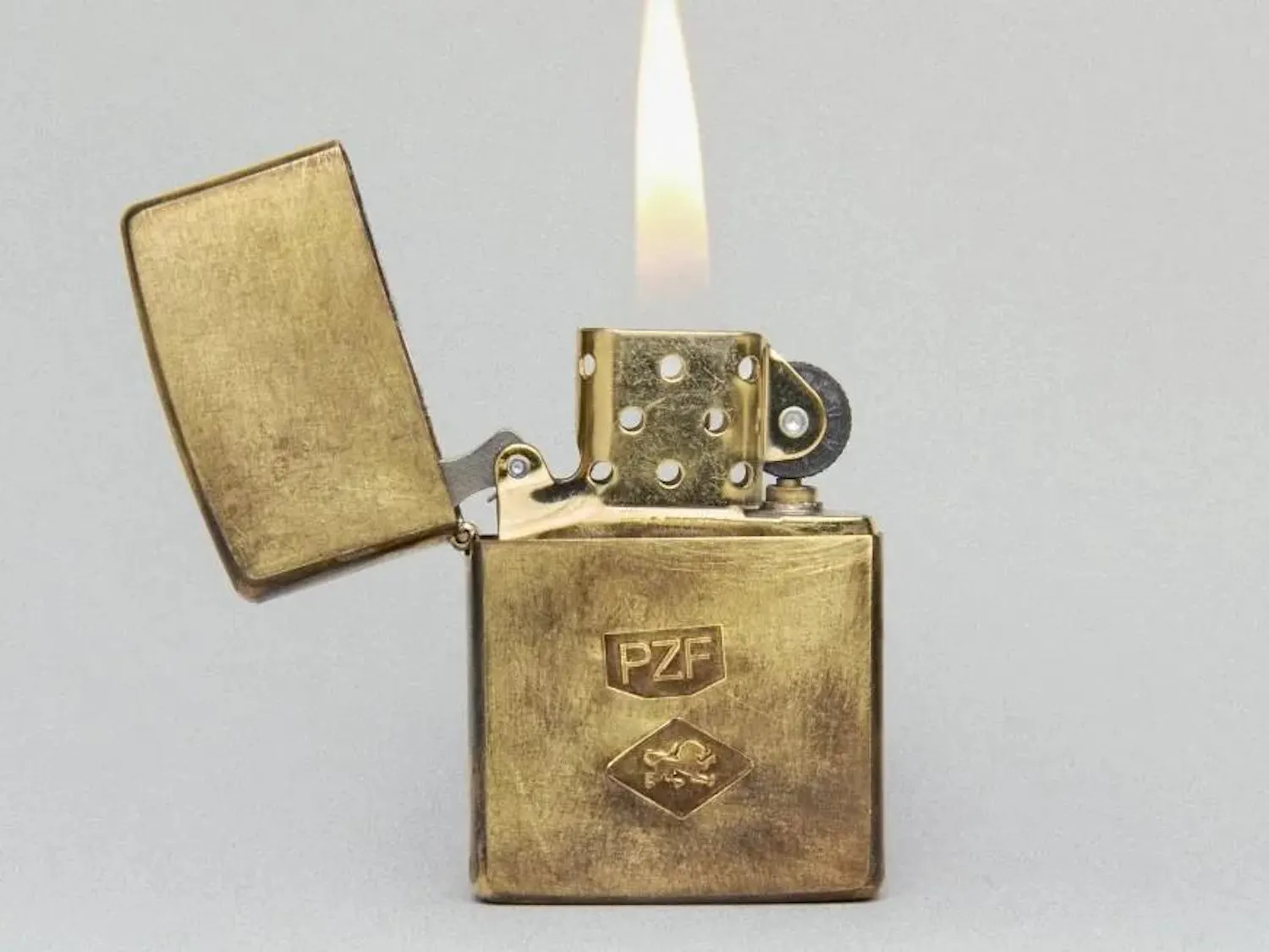 A close-up photo of a lit gold Zippo lighter, with the letters PZF engraved on it.