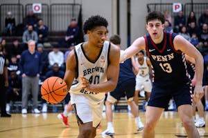 Lewis on the basketball court mid-game. He is holding a basketball and a player wearing a University of Pennsylvania jersey is guarding him.