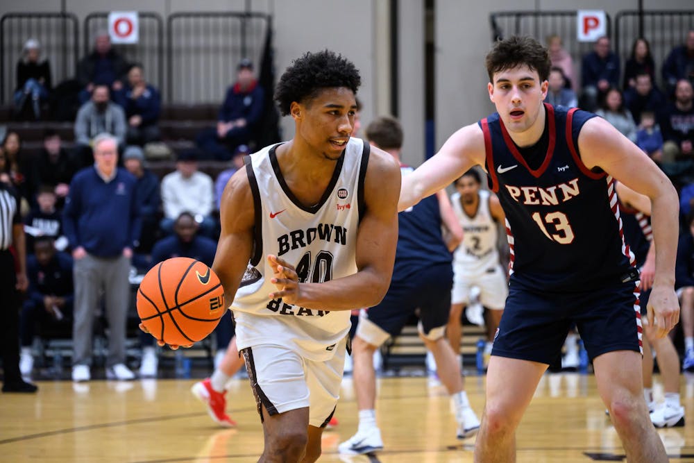Lewis on the basketball court mid-game. He is holding a basketball and a player wearing a University of Pennsylvania jersey is guarding him.