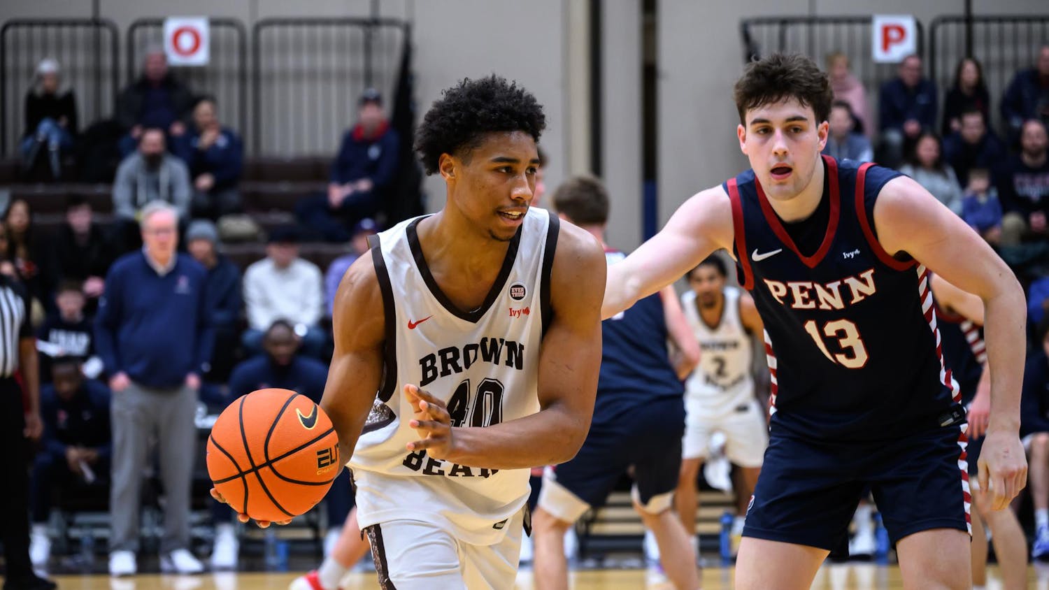 Lewis on the basketball court mid-game. He is holding a basketball and a player wearing a University of Pennsylvania jersey is guarding him.