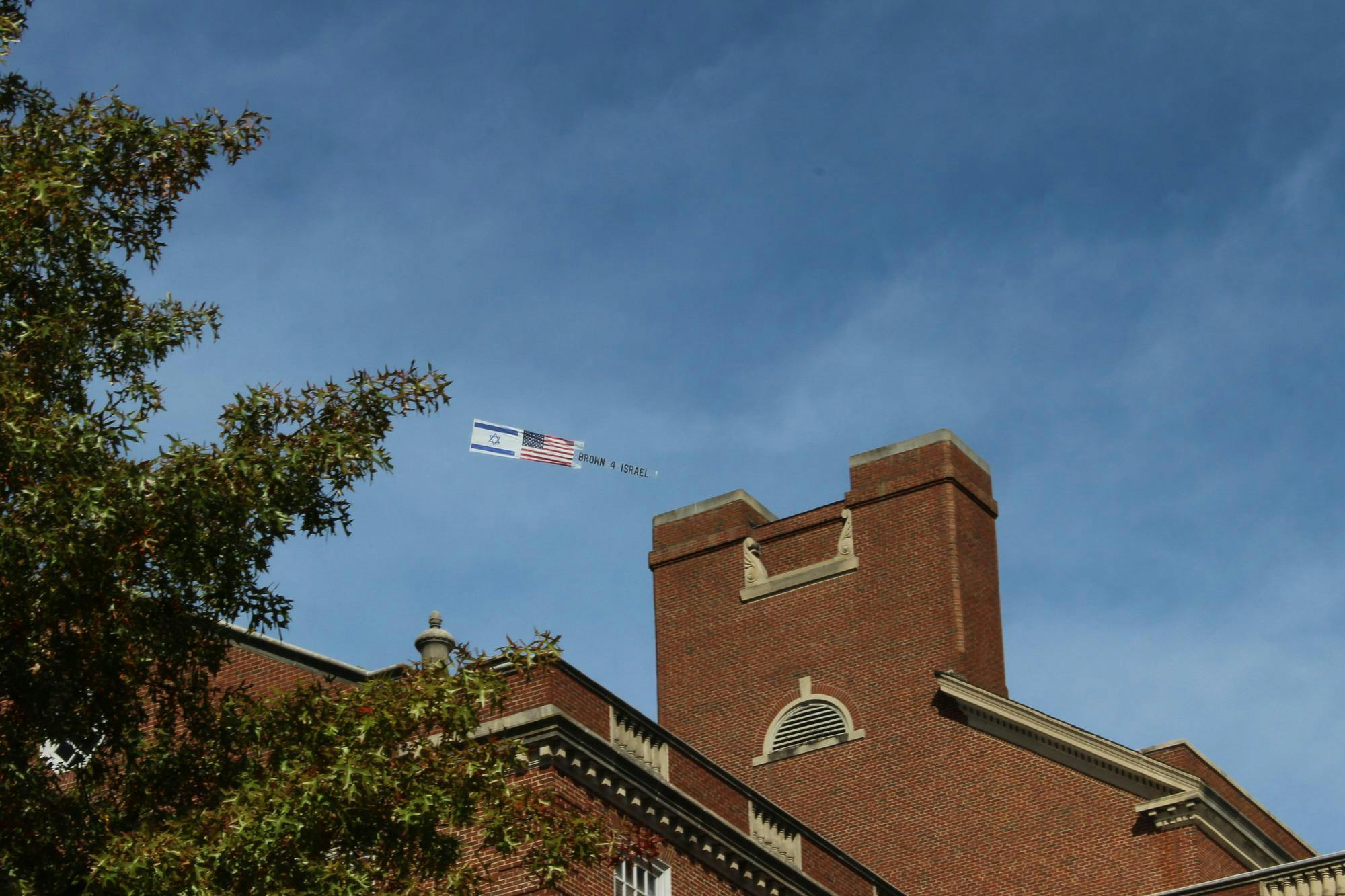 Photo of a building with a plane in the background with the Israeli and American flag in front of the words “Brown 4 Israel.”