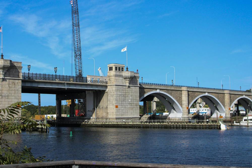 Photo showing the stone Washington Bridge over a river with two construction cranes in the background. 