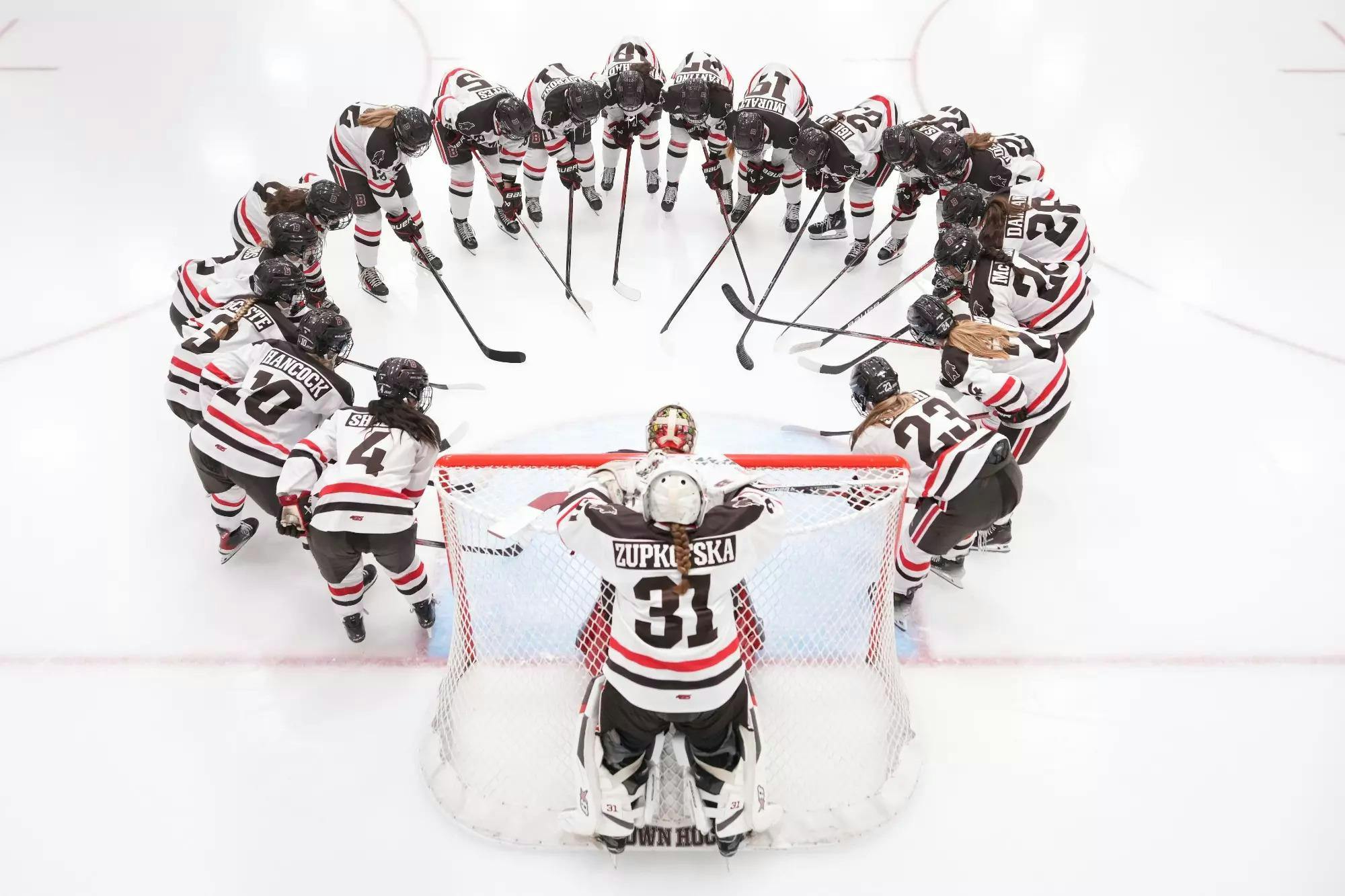 The women's hockey team huddles with their hockey sticks in a large circle.