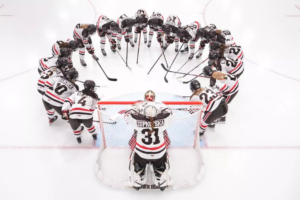 The women's hockey team huddles with their hockey sticks in a large circle.