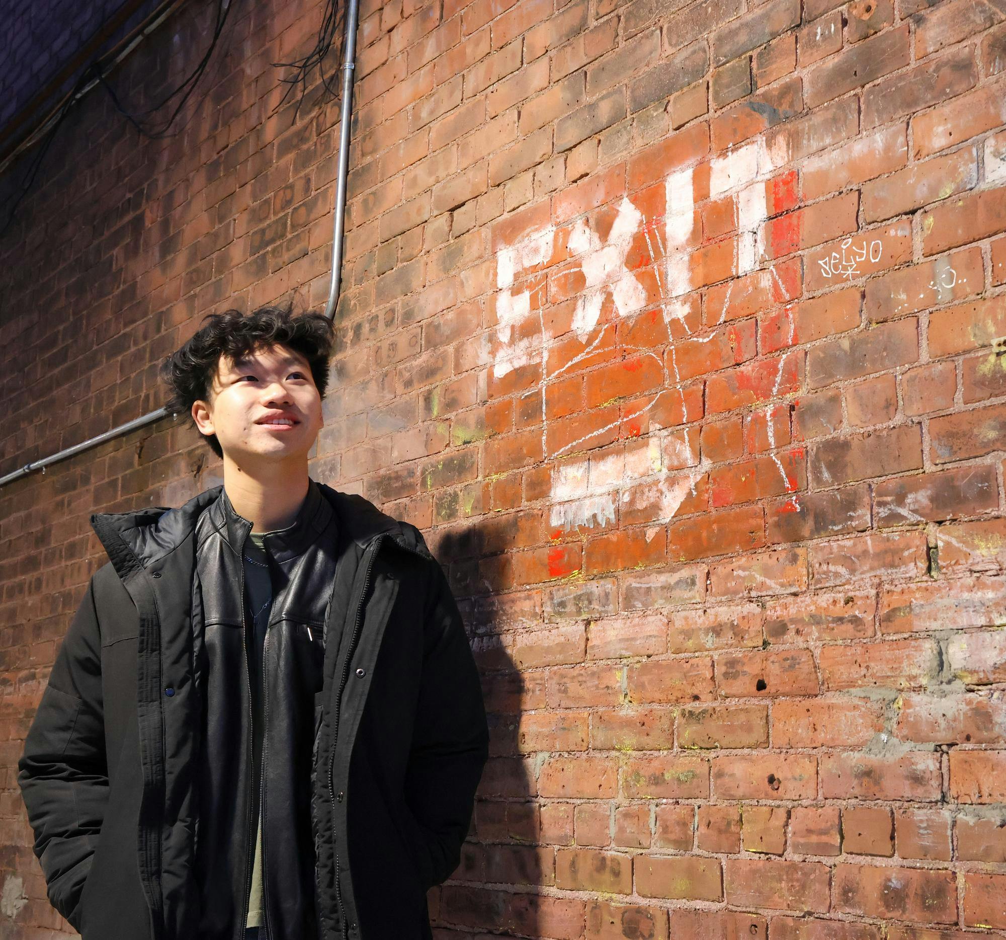 Man in black puffer jacket looking up with a brick background.