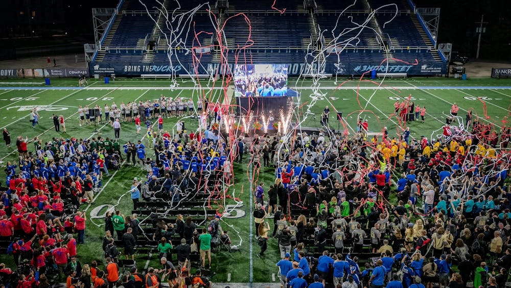 Crowds of athletes stand in a stadium as multicolored confetti and fireworks explode into the air.