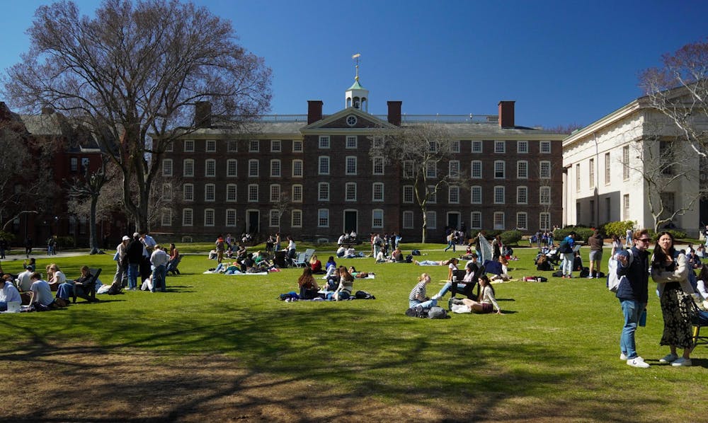Brown University's Main Green, a large lawn featuring a large brick building in the background with many students sitting on the grass with blankets.