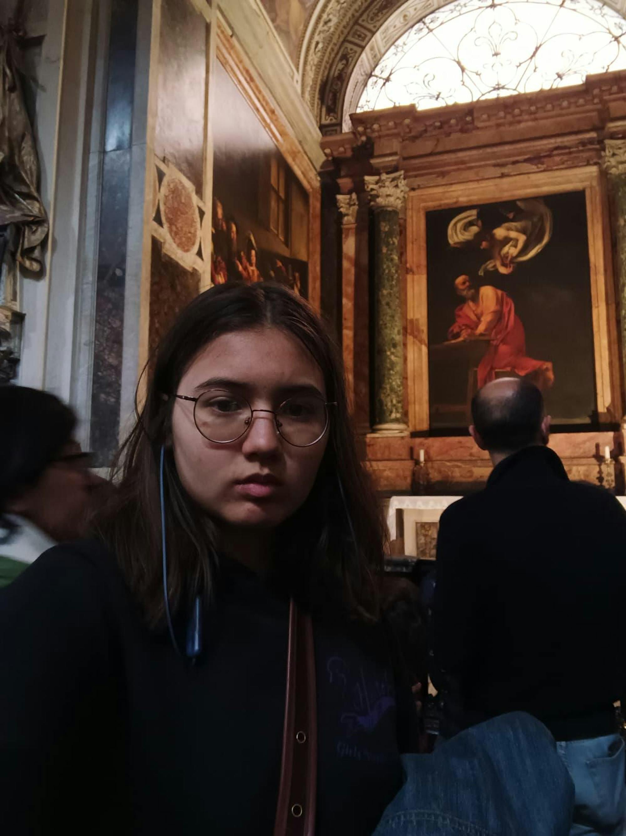 A girl with glasses stands in an art museum. 