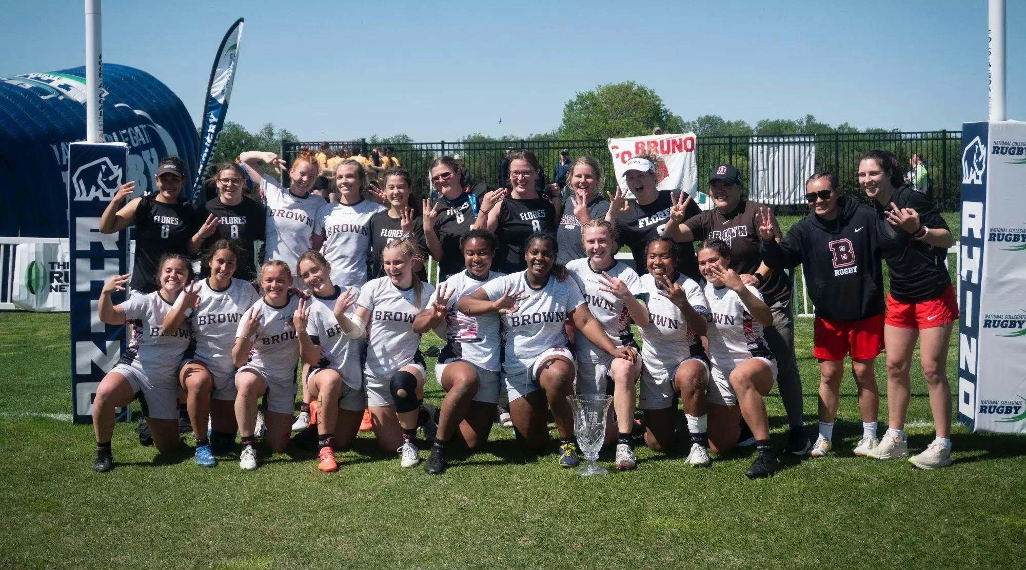 A photo of the Women's Rugby Team celebrating their third national championship. Each member of the team is holding up three fingers.