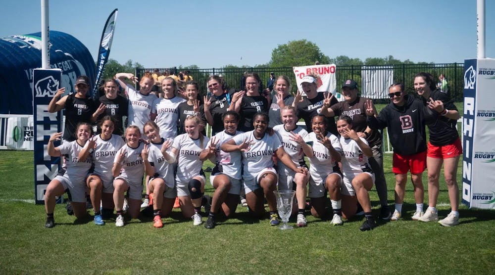 A photo of the Women's Rugby Team celebrating their third national championship. Each member of the team is holding up three fingers.