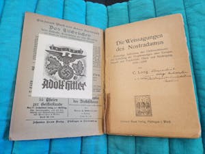 An open title page to "The Prophecies of Nostradamus," with handwritten lettering under the words "Die Weissagungen des Nostradamus." On the left page, there is a paper attachment that states "Ex Libris Adolf Hitler" with Nazi party symbolism and a swastika.