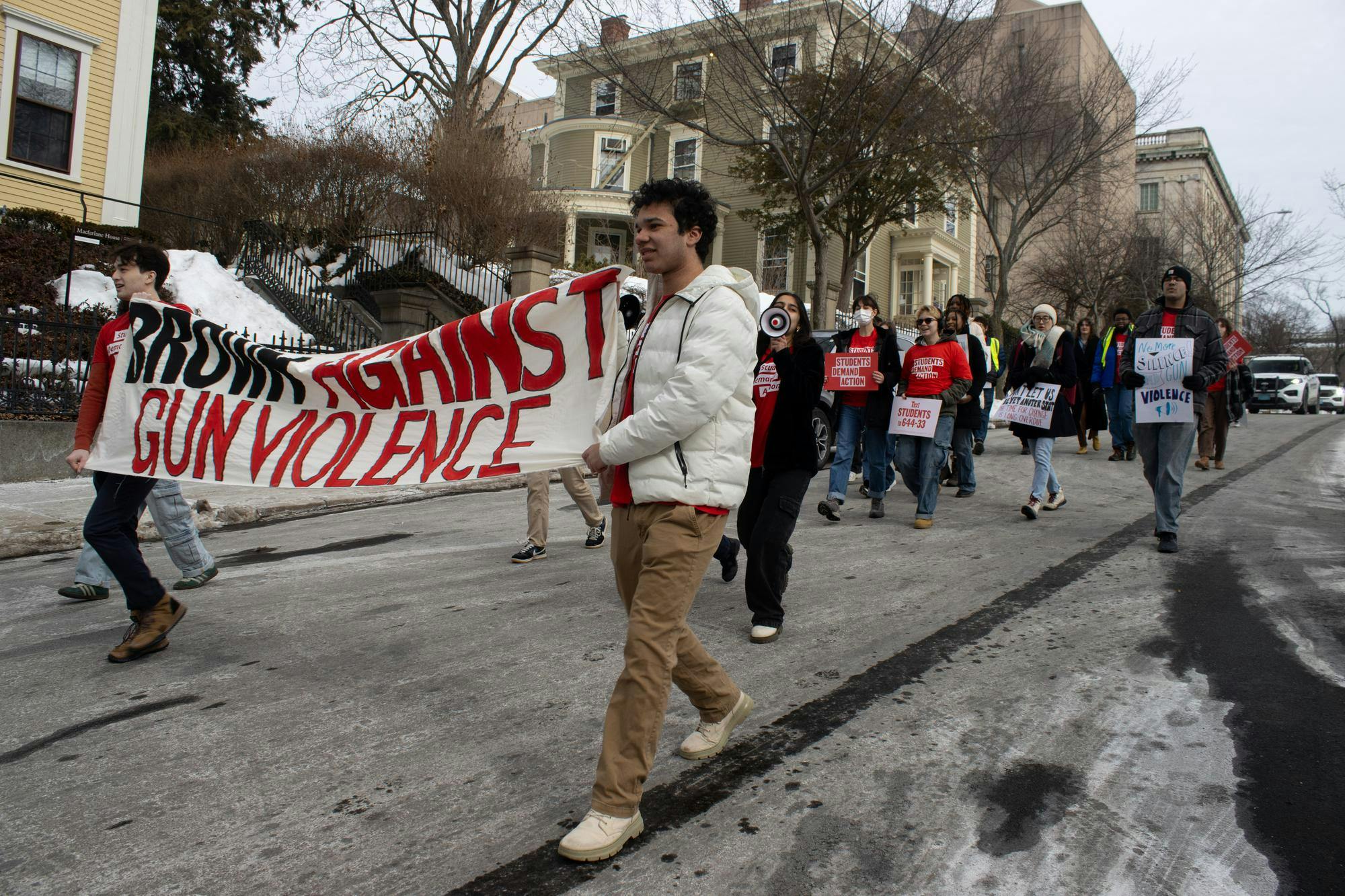 A photo from the protest with SDA members wearing the club's red t-shirts, holding posters, microphones and a long banner saying “Brown Against Gun Violence.”

