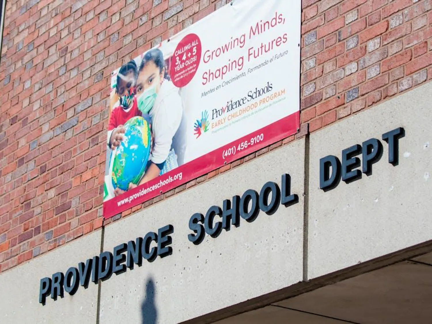 A picture of a brick building that says "Providence School Department" with a banner of children in masks above.