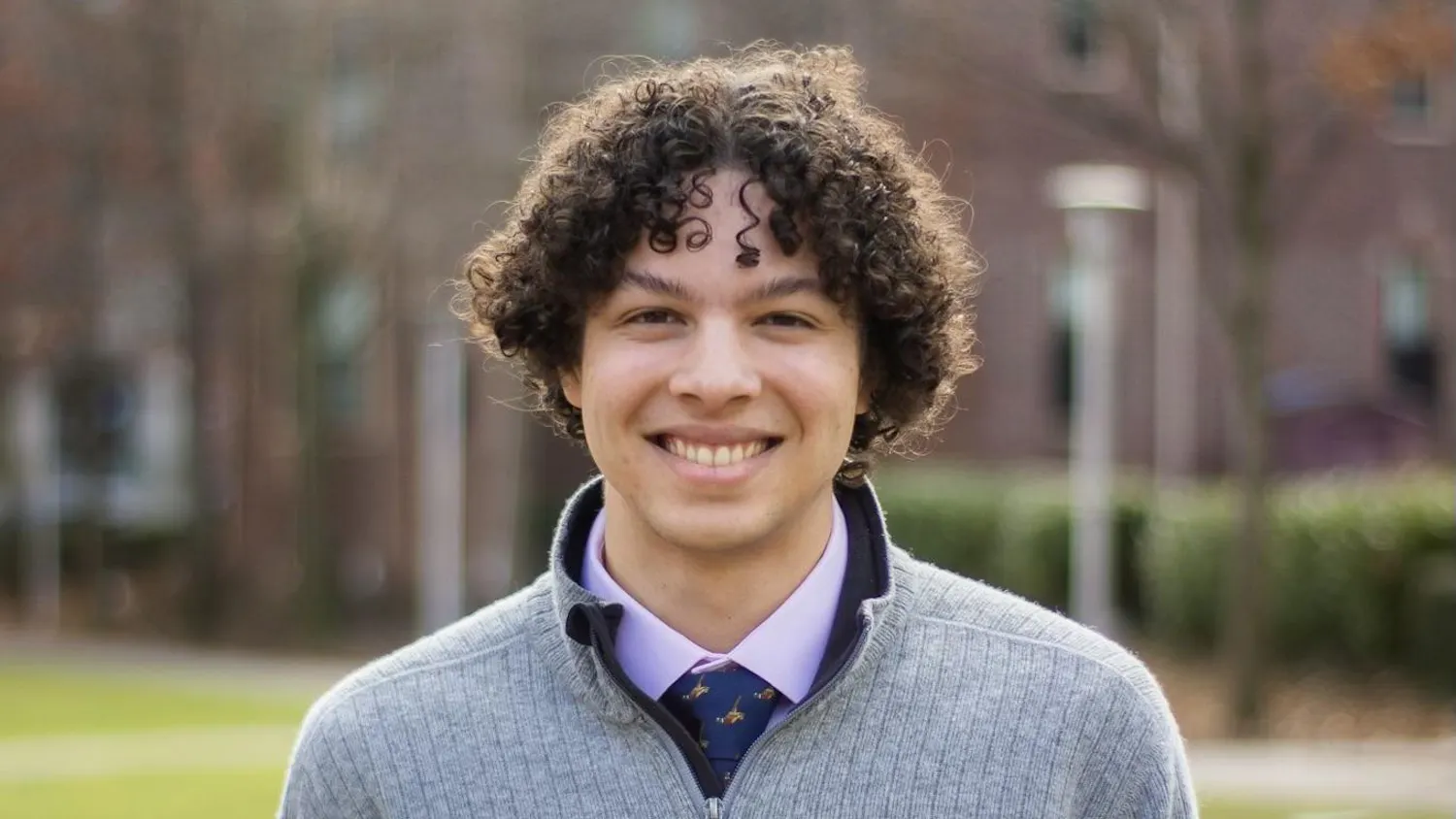 A headshot picture of Eric Gottlieb '25 wearing a gray quarter-zip sweater with a pink collared shirt and blue necktie underneath.