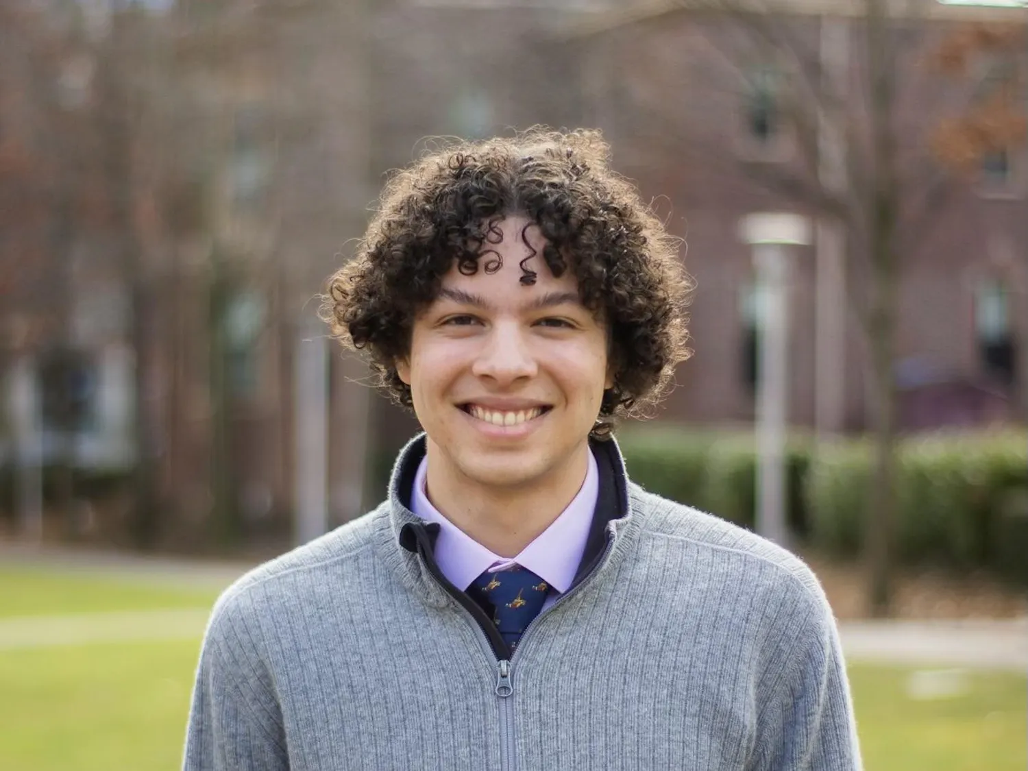 A headshot picture of Eric Gottlieb '25 wearing a gray quarter-zip sweater with a pink collared shirt and blue necktie underneath.
