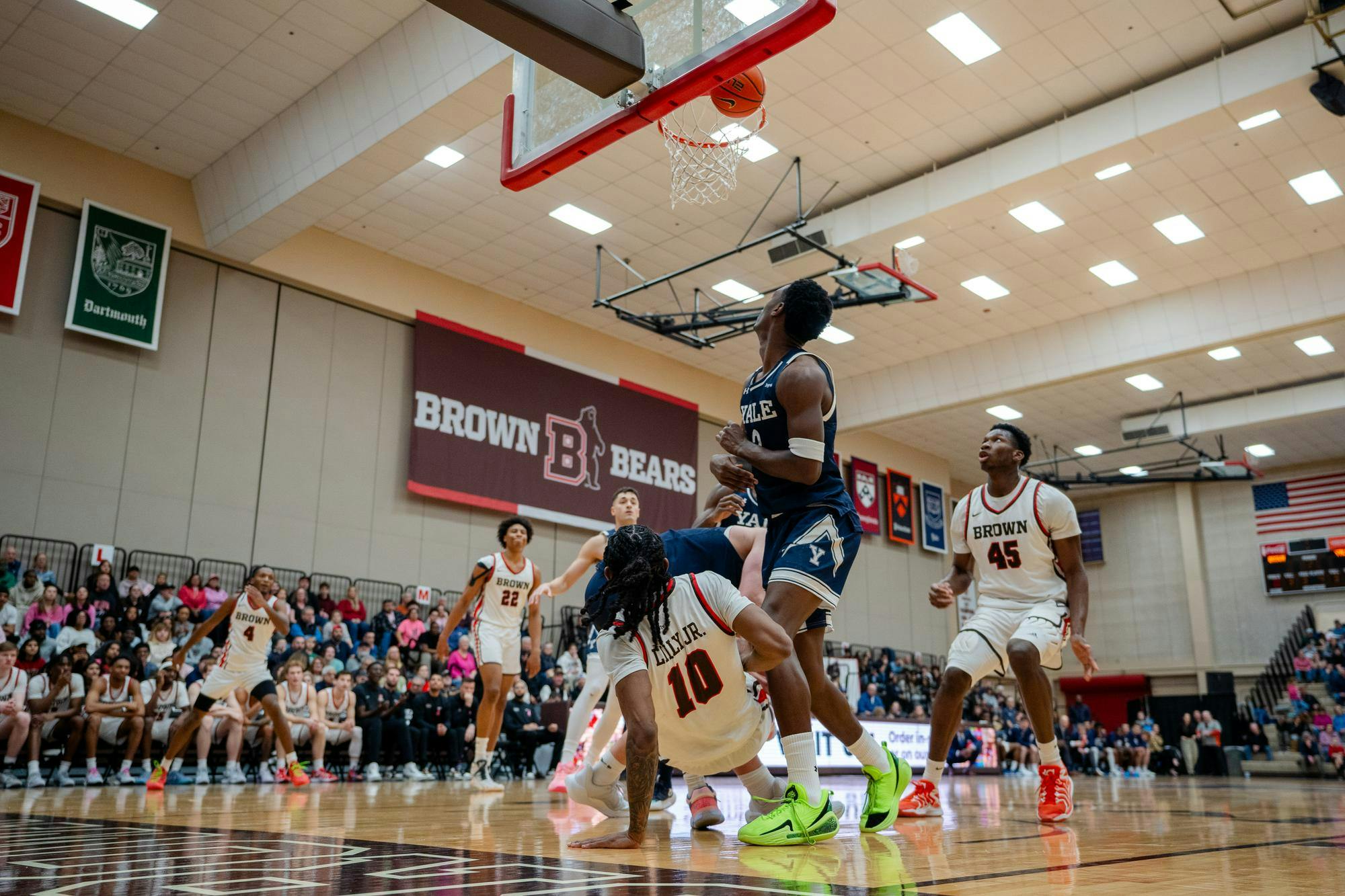 A picture of basketball players from Brown and Yale watching as a ball nears the hoop.