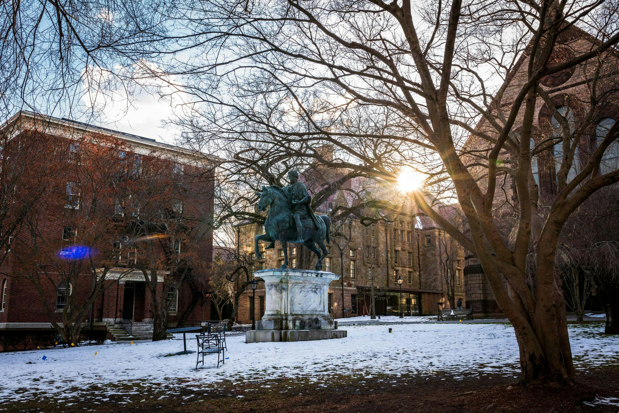 Statue of Marcus Aurelius in the middle of Brown’s snowy campus as the setting sun shines through the surrounding buildings. 
