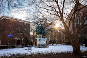 Statue of Marcus Aurelius in the middle of Brown’s snowy campus as the setting sun shines through the surrounding buildings. 