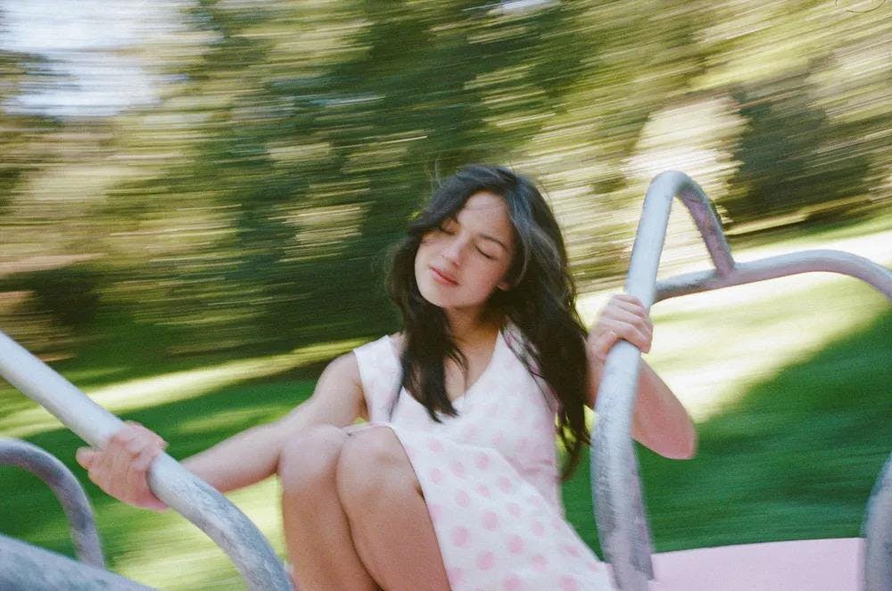 A promotional photograph of Olivia Rodrigo spinning on a playground merry-go-round.