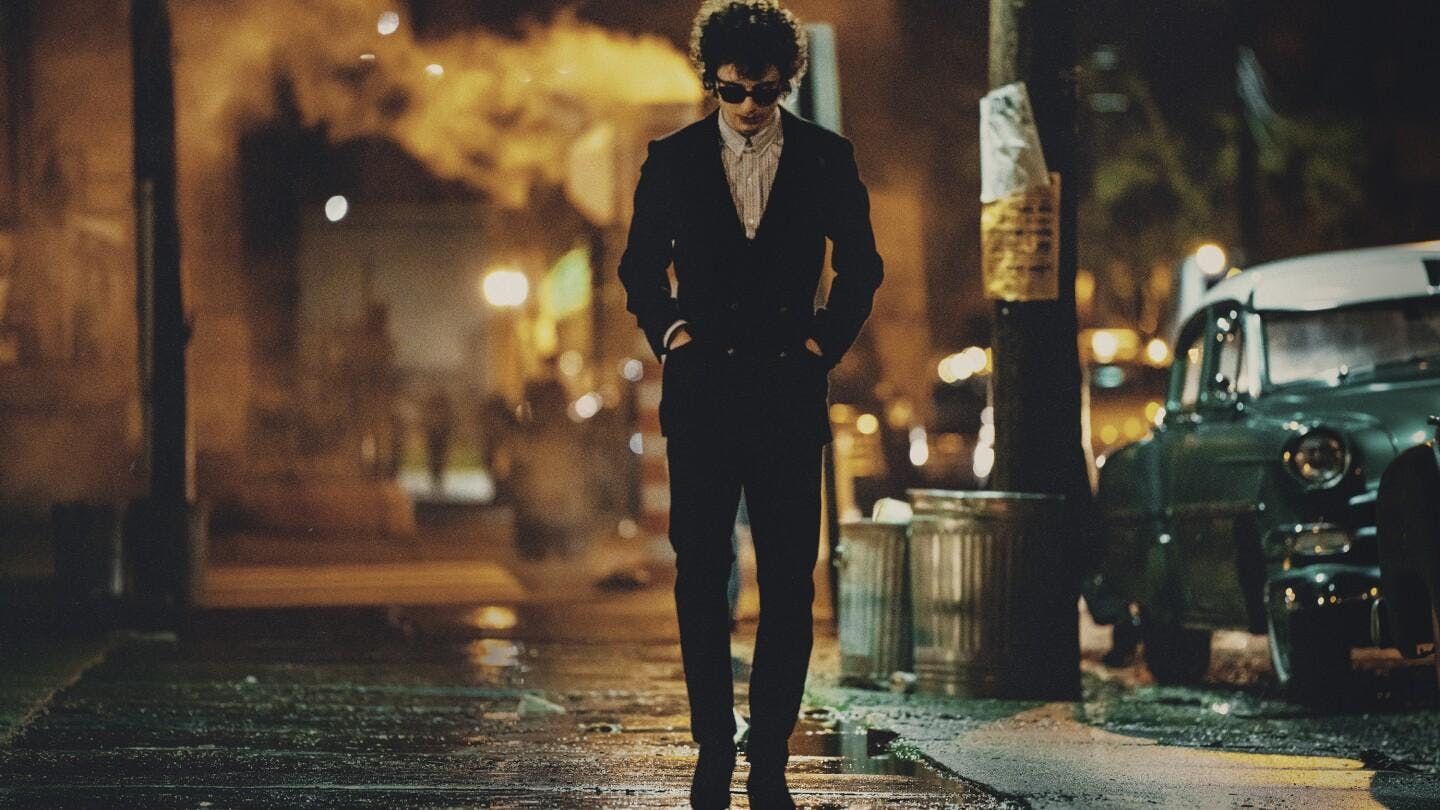 An image of Timothée Chalamet with sunglasses walking through a wet street.