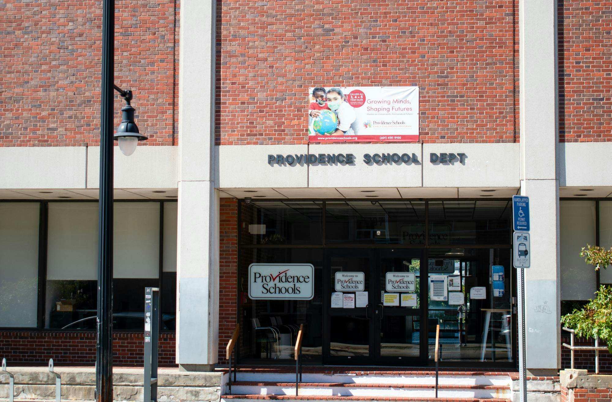 A photo of the front of a brick building that says “Providence School Dept.” with a black lamp to the left of the entrance. 
