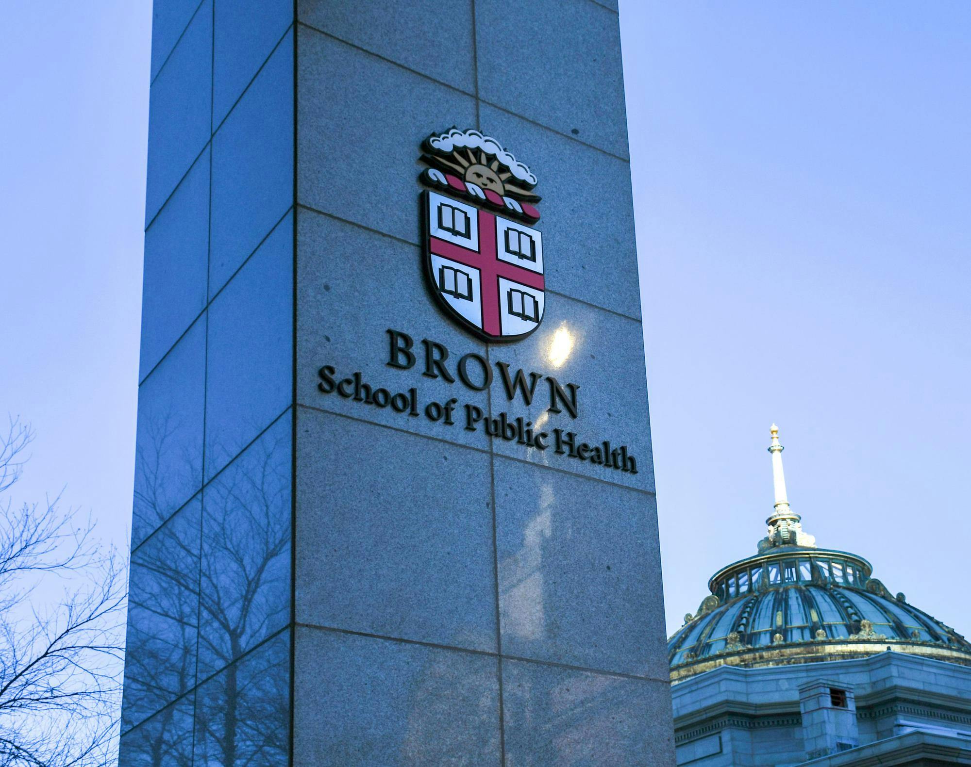 A gray column with the Brown university, a red and white crest with a sun, that says "Brown School of Public Health" underneath.