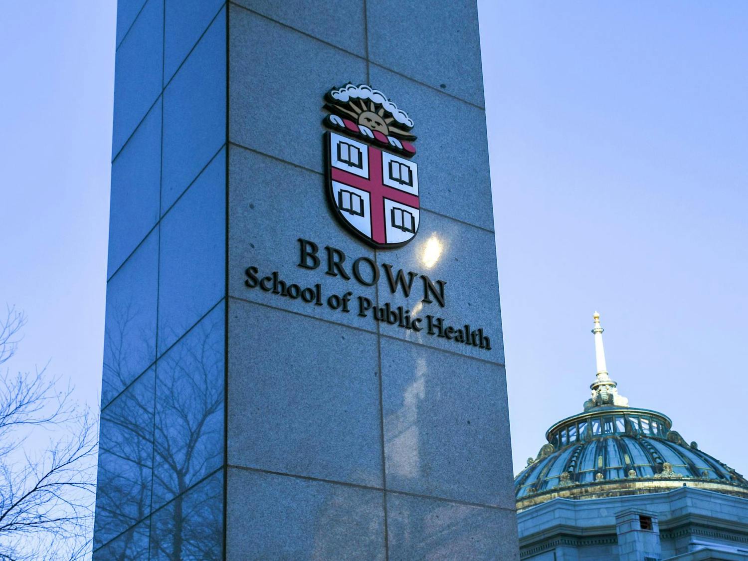 A gray column with the Brown university, a red and white crest with a sun, that says "Brown School of Public Health" underneath.
