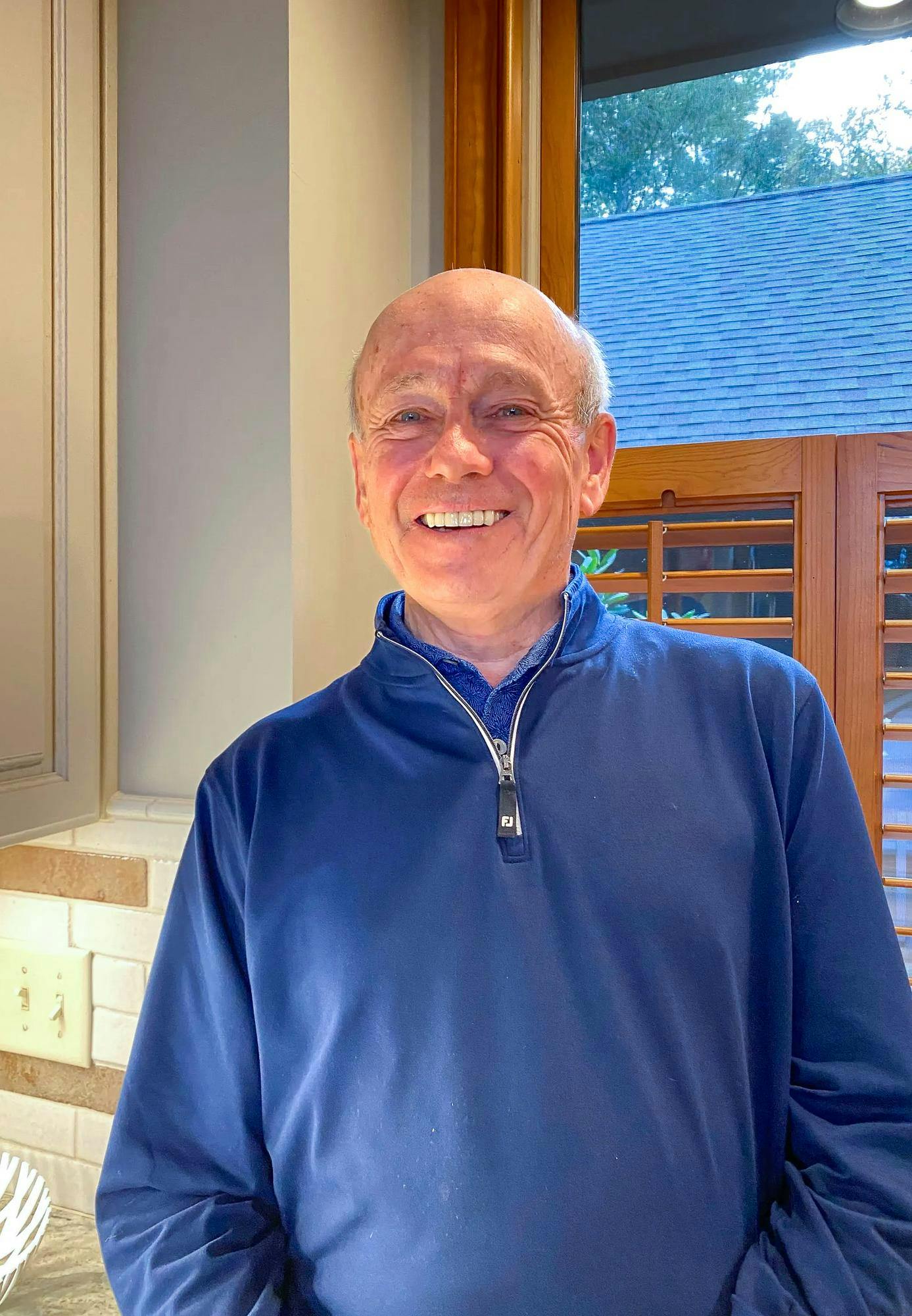 A man with white hair wearing a blue shirt smiles into the camera.