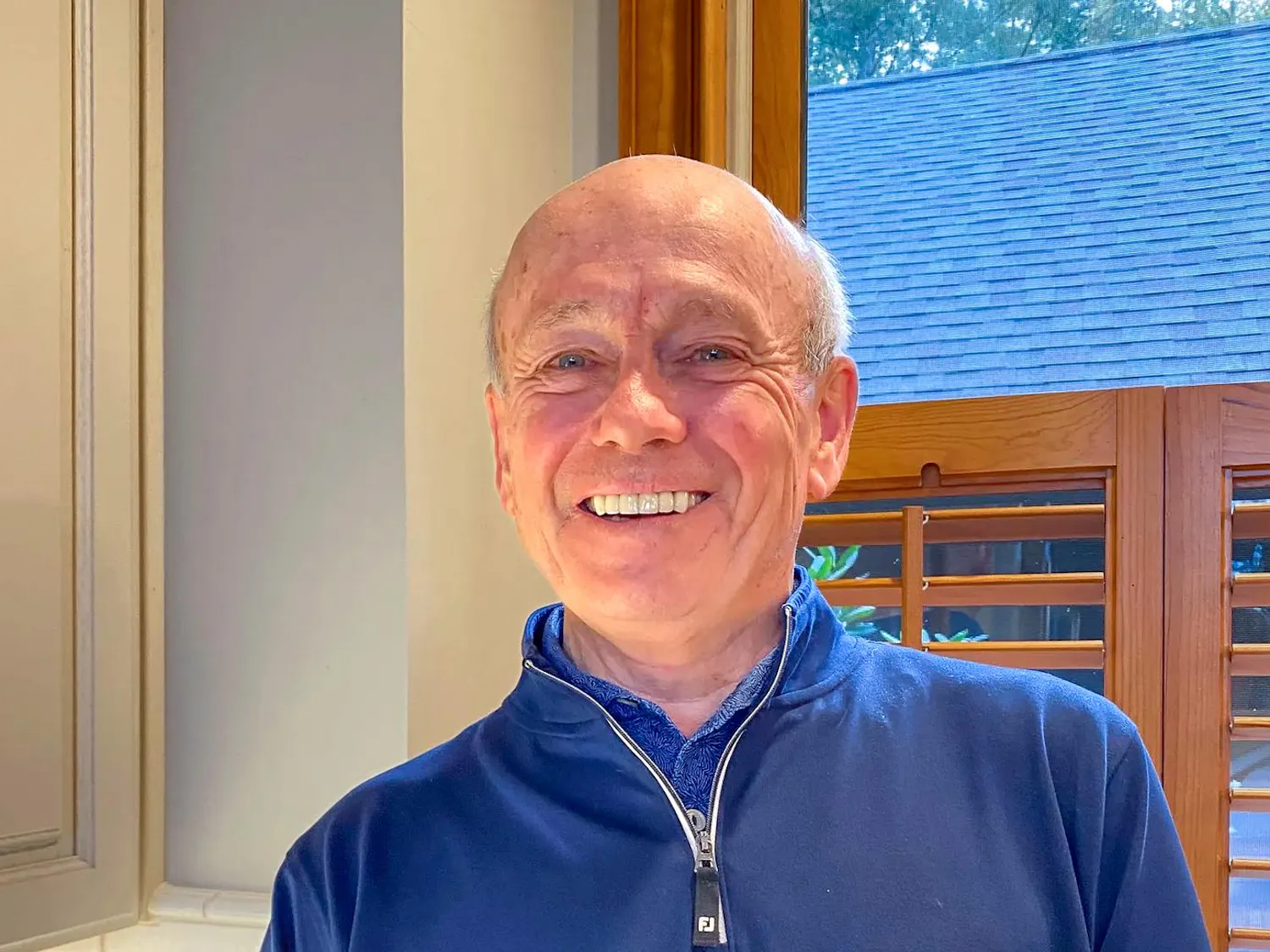 A man with white hair wearing a blue shirt smiles into the camera.