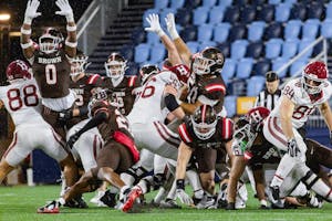 A tableau photograph of Harvard and Brown football players during a play. Some are reaching into the air, while others are mid-stumble. 