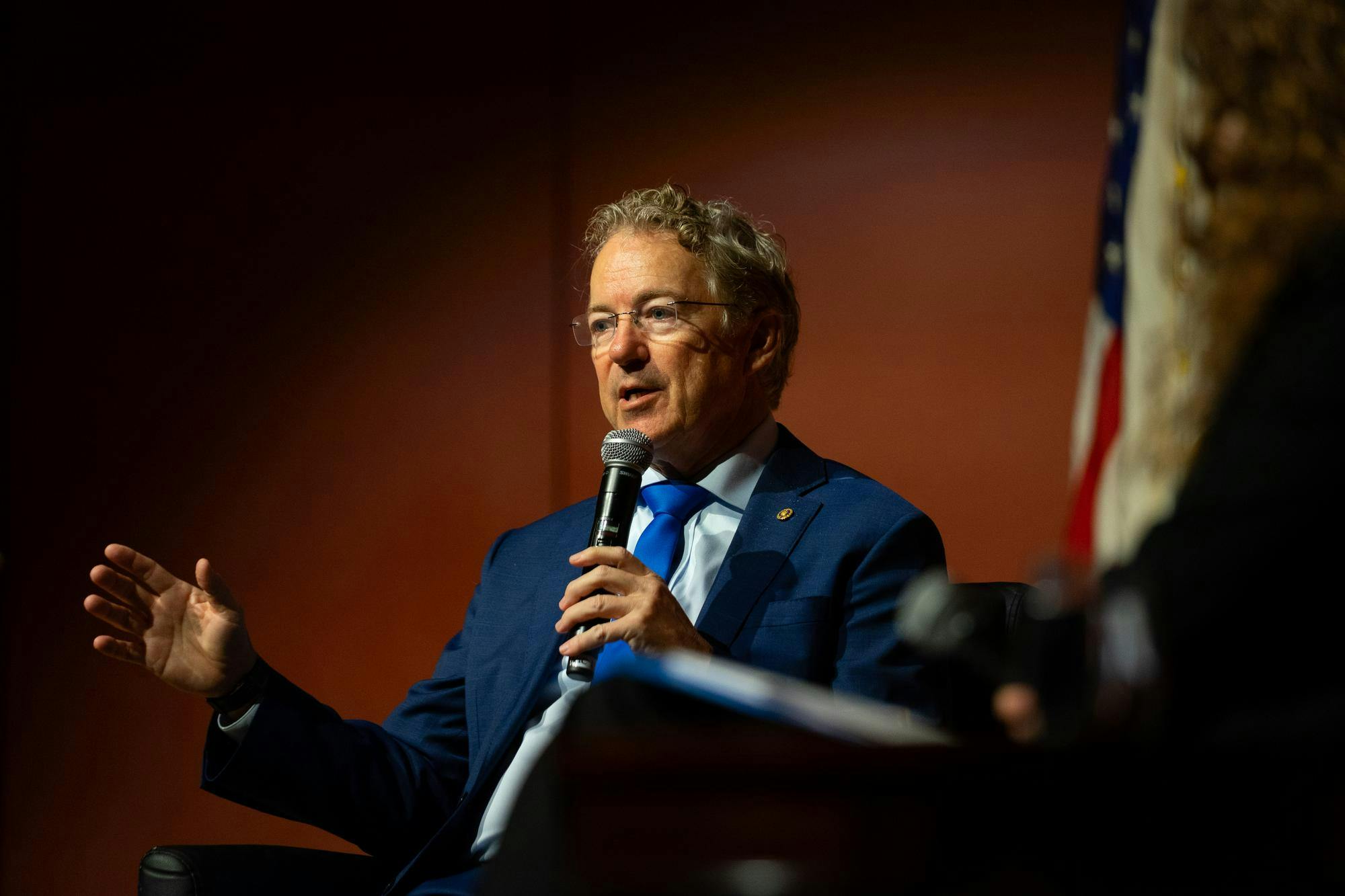 U.S. Sen. Rand Paul, a gray-haired man with glasses and a navy blue suit, solemnly speaks into a microphone onstage.