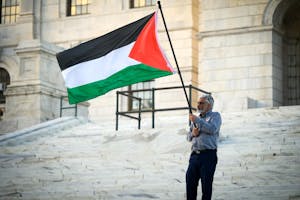 Photo of a man in front of the Rhode Island State House holding a Palestinian flag.