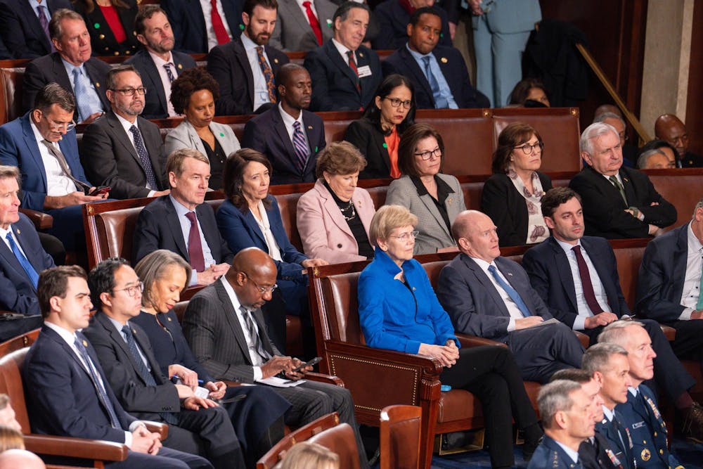 People in official attire seated in multiple rows of brown leather chairs in the House Chamber with an attentive expression on their faces. 