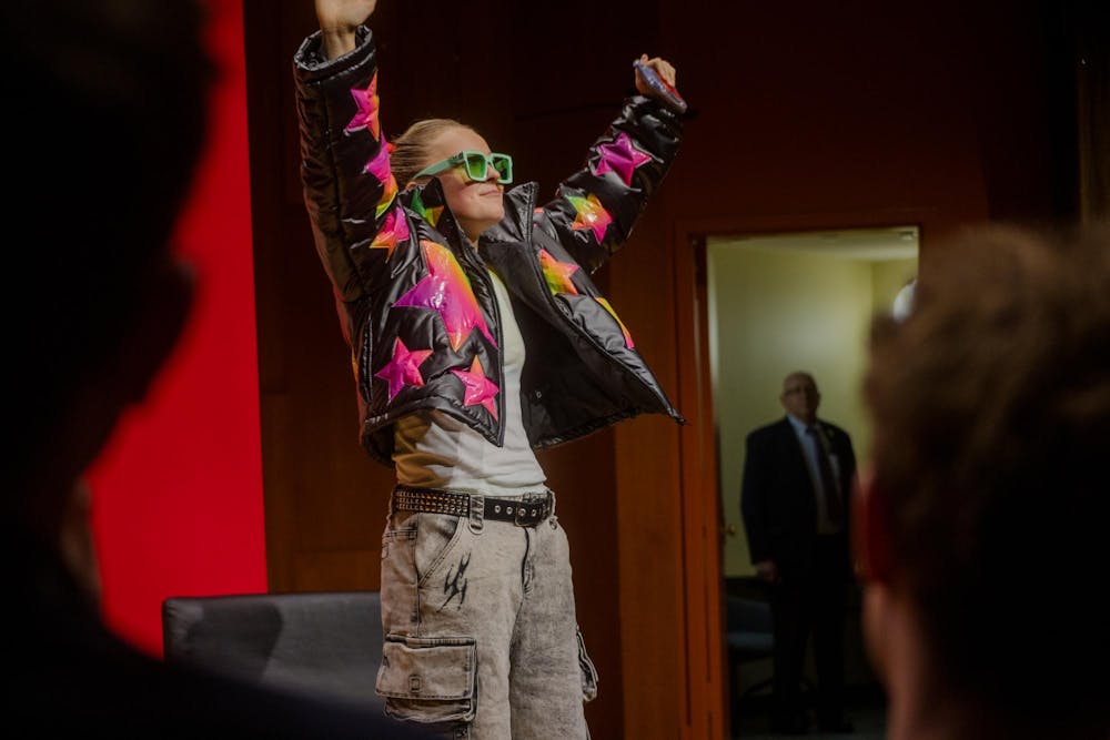 JoJo Siwa stands on the Salomon DECI stage at Brown University in a black jacket with rainbow stars. 